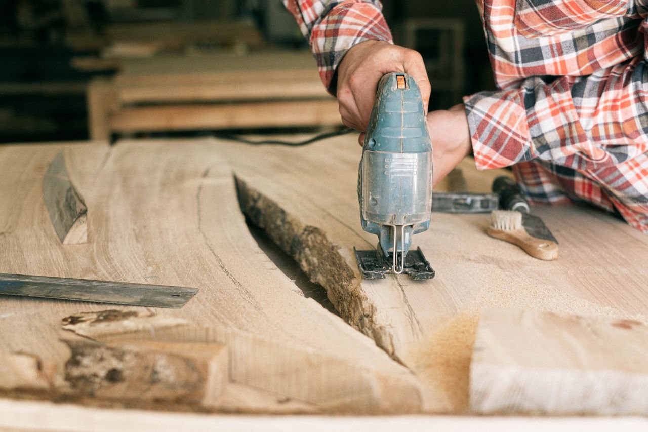 Close-up of a carpenter cutting a wooden plank with a power tool in a workshop.