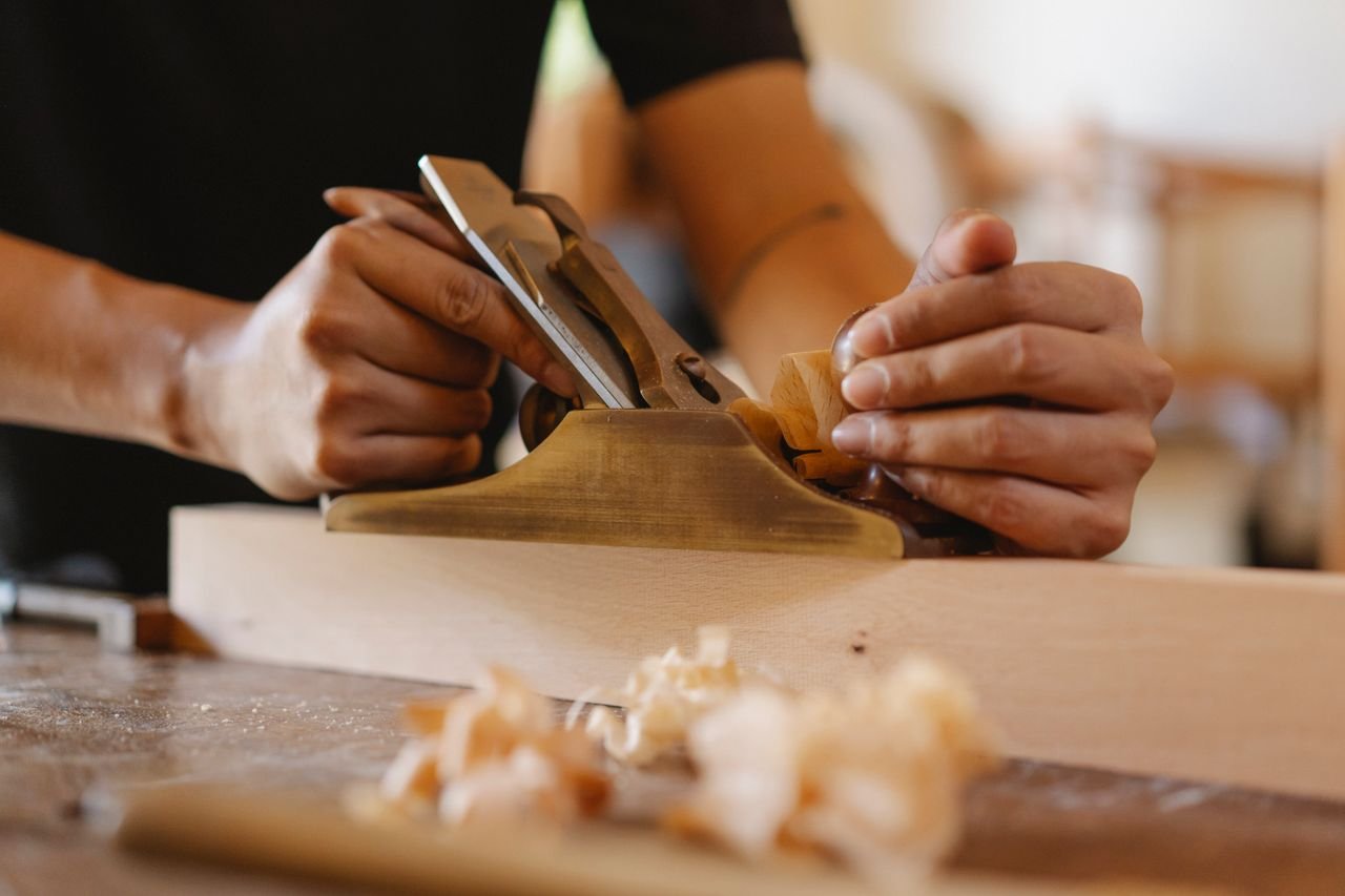 Crop faceless male carpenter shaping wooden board using jack plane during work in studio